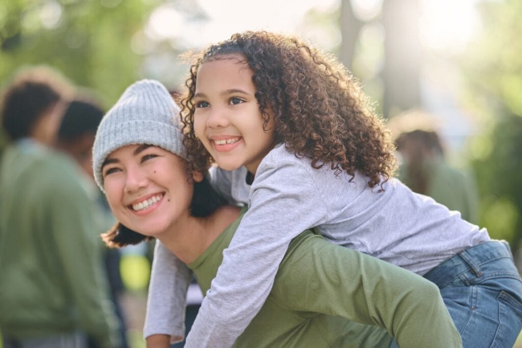 smiling woman giving smiling young girl a piggyback ride