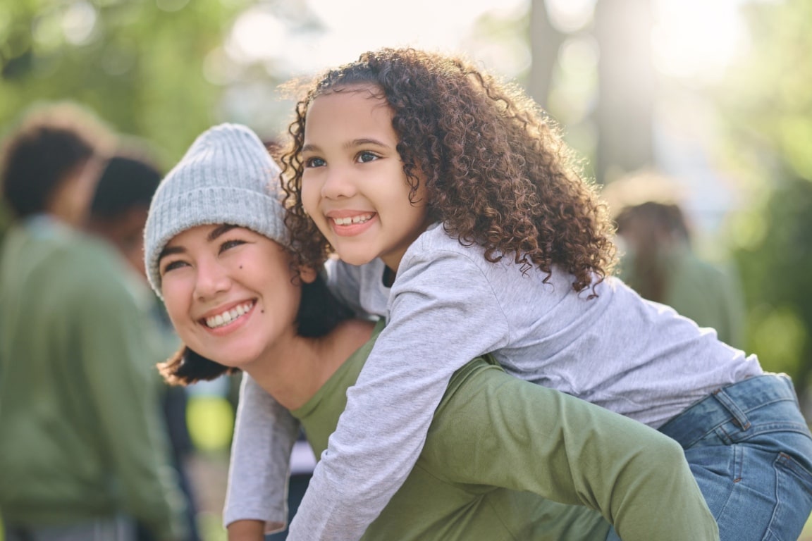smiling woman giving smiling young girl a piggyback ride